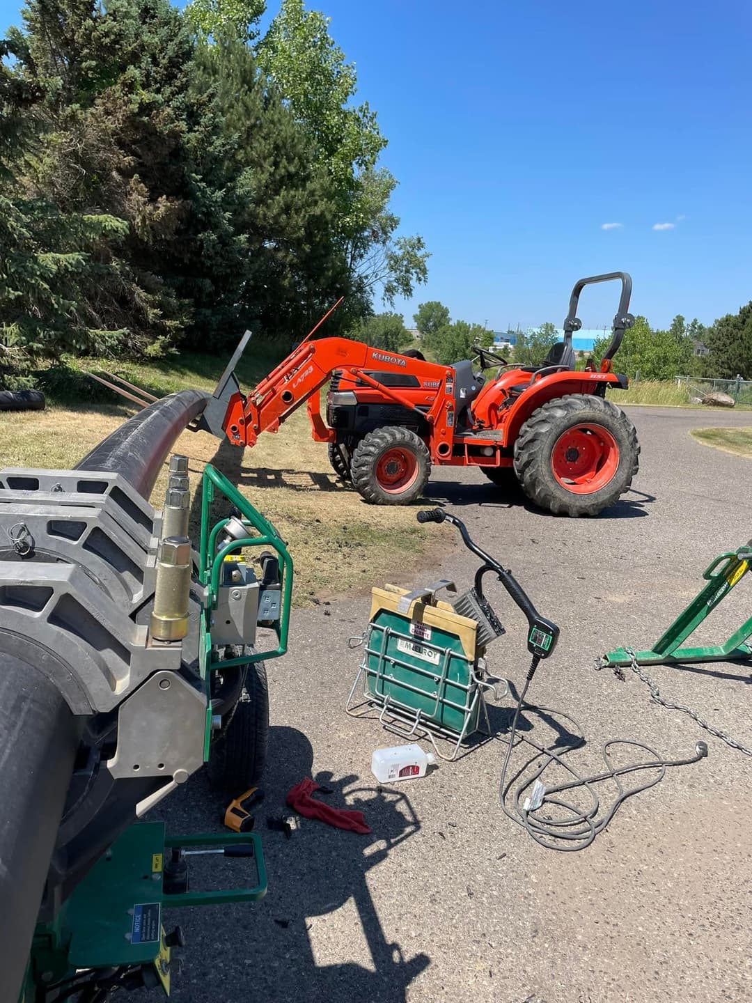 Kubota tractor with loader parked near freshly cut grass and tools on a sunny day.